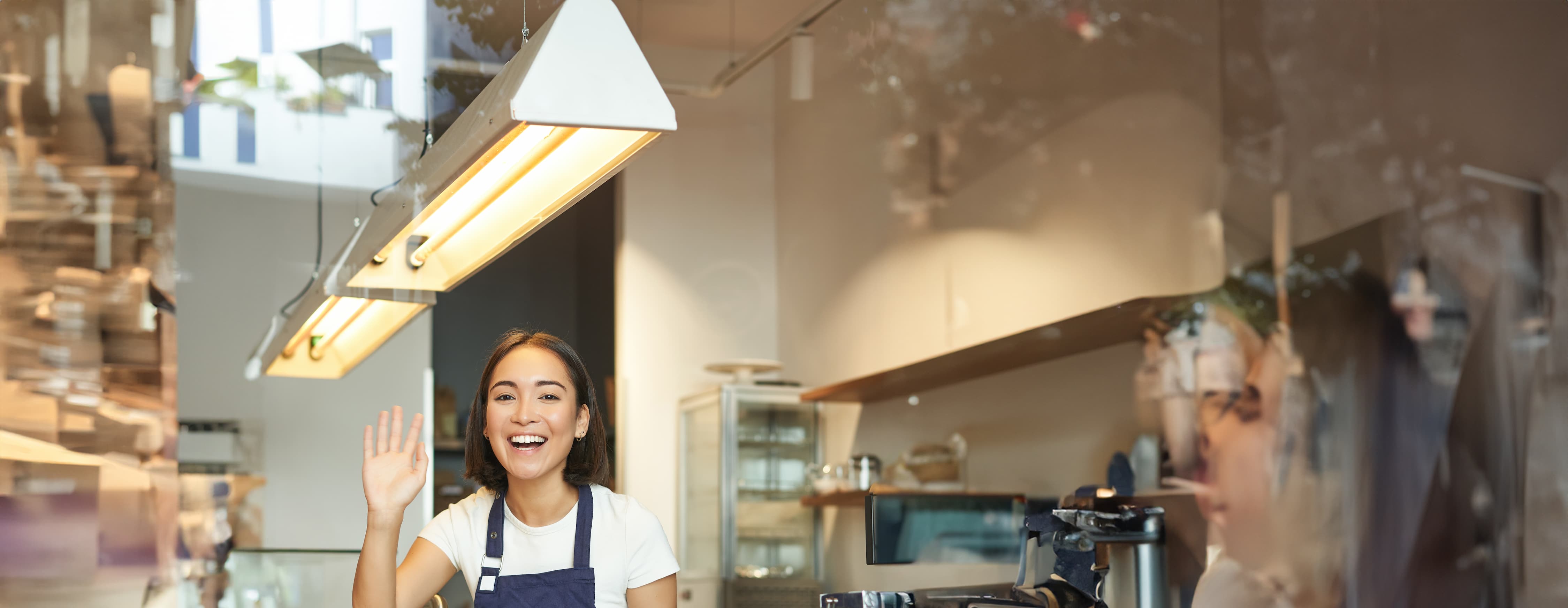 happy-asian-girl-barista-works-coffee-shop-waves-client-processing-orders-counter.jpg